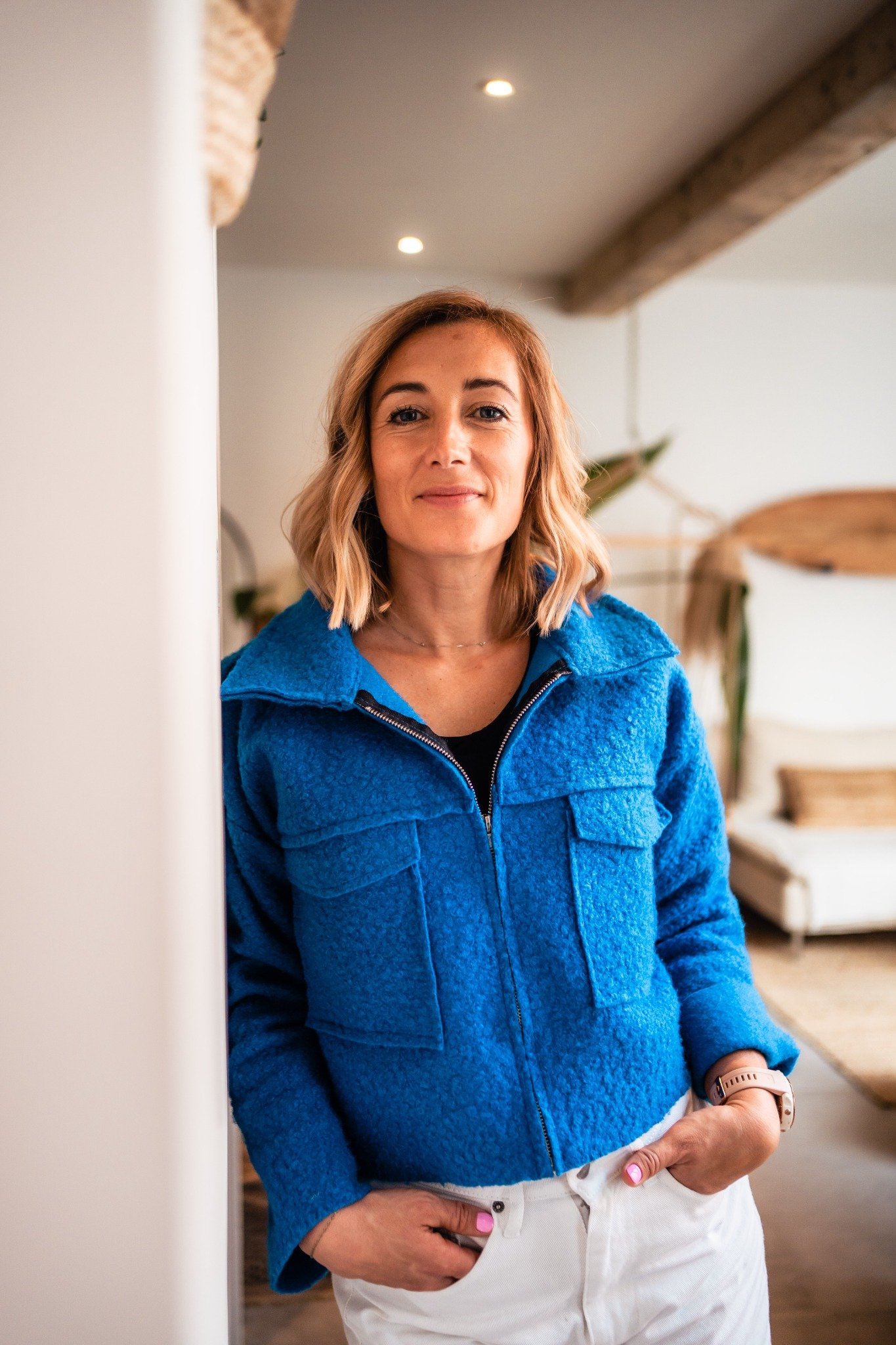 Sophie Couillard en veste bleue, appuyée contre un mur dans un intérieur lumineux